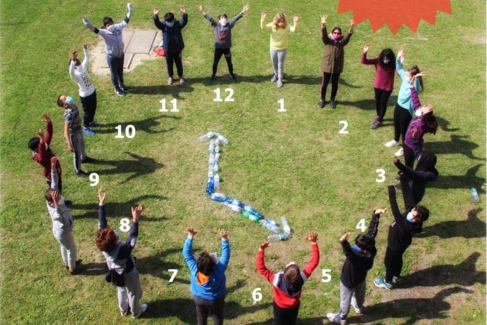 studenti per mano in cerchio in piedi sul prato con lancette e orologio creato nel mezzo, fotografia dall'alto