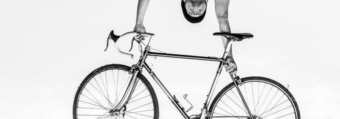 fotografia b/n uomo che solleva in alto bicicletta da corsa